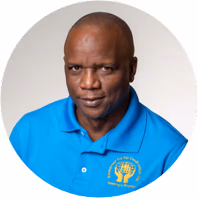 Portrait of a man wearing a blue polo shirt with a logo, smiling slightly against a white background.