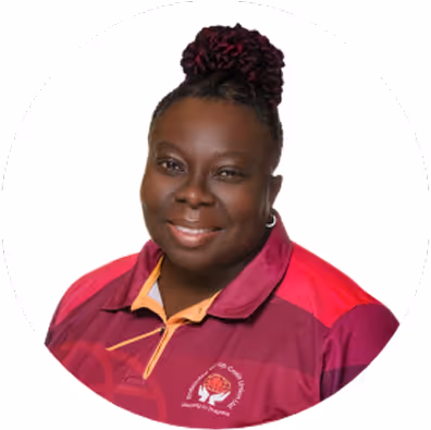 Smiling woman with braided hair styled in a bun, wearing a maroon and red collared shirt with a logo on it, against a white background.